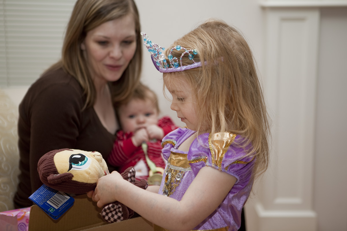 Maddi opening another present while Mommy & Thomas look on
